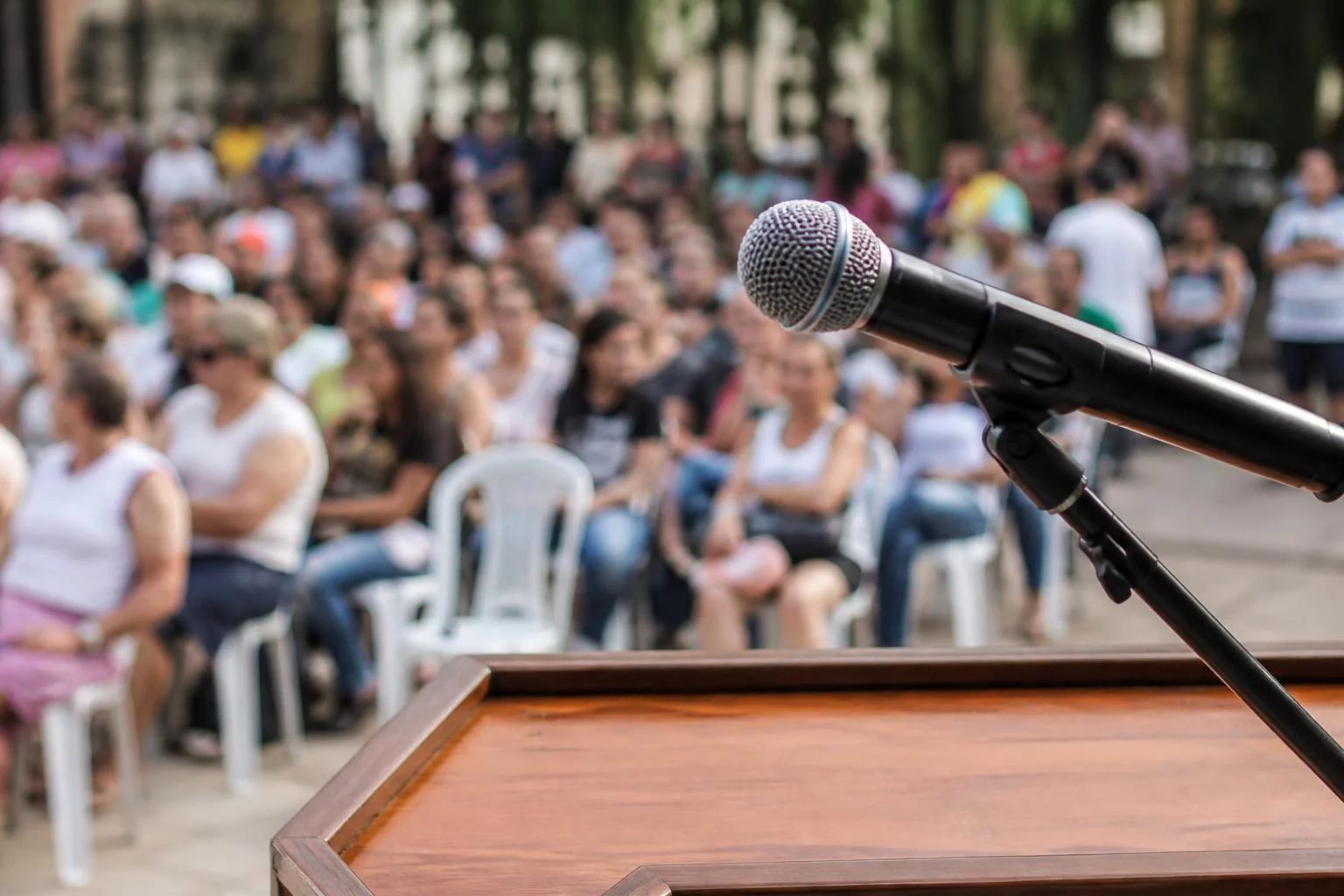 Microfone sobre uma tribuna, com a plateia sentada desfocada ao fundo